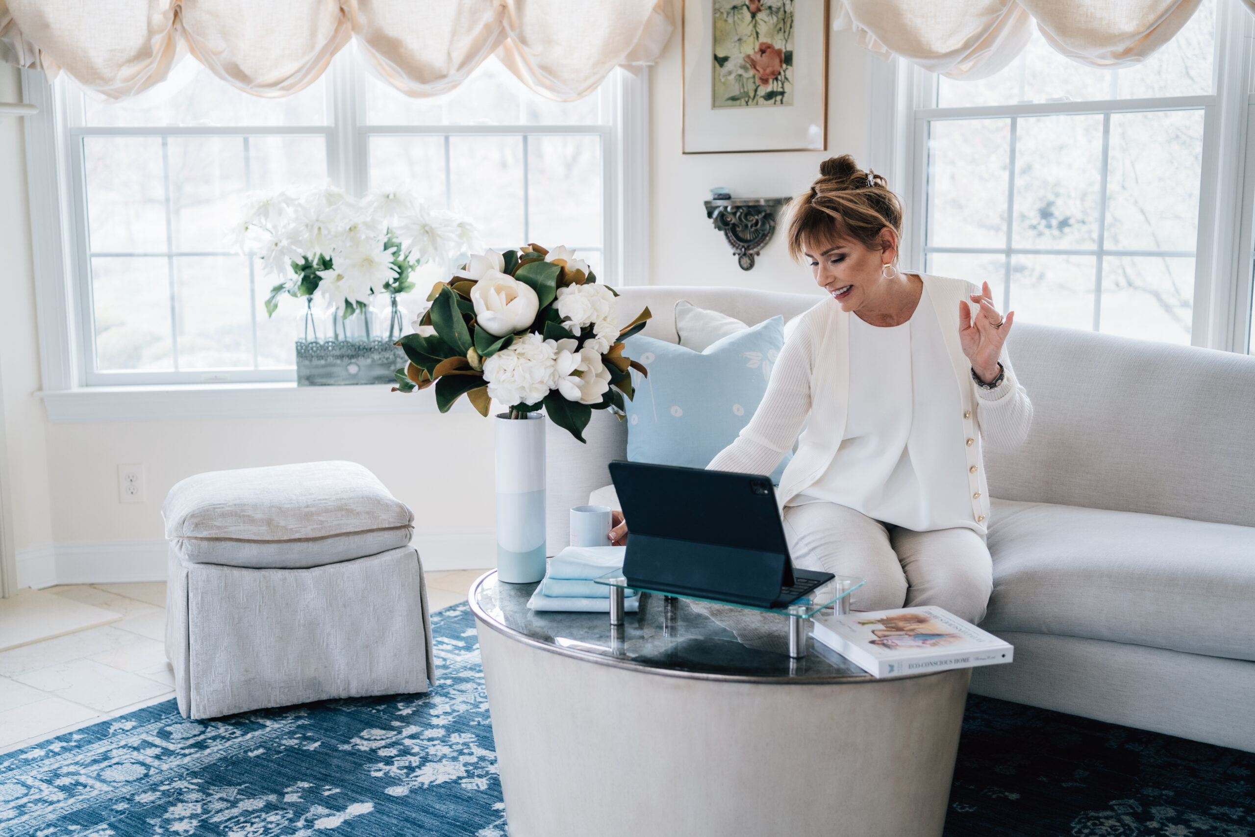 Charisse Marei working from home on a laptop while seated on a sofa surrounded by natural light, fresh flowers, and a thoughtfully designed workspace.